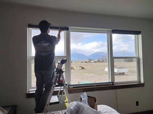 Man standing on a short ladder installing blinds.