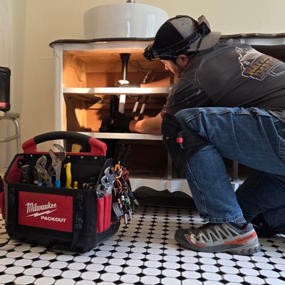 White man installing plumbing fixtures for a bathroom sink.