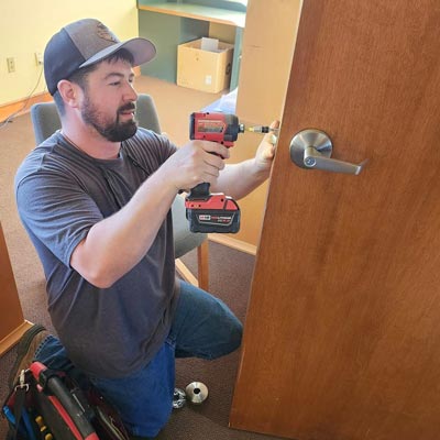 White man with dark gray shirt installing a door knob on a wooden door. 