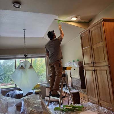 Man on a step stool painting the ceiling. 