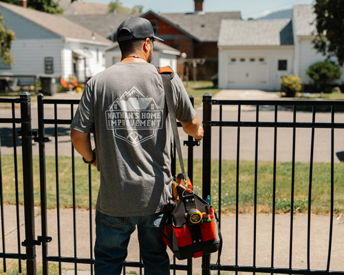 Man wearing a grey Nathan's Home Improvement shirt entering a yard through the front gate.