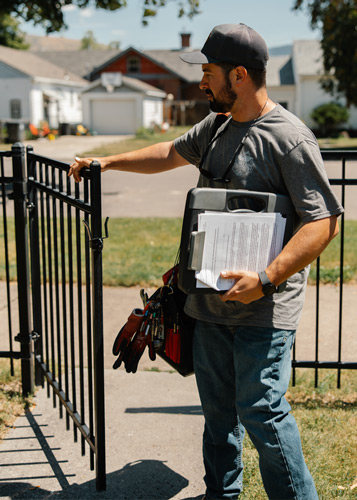Man entering through a gate. He's holding a clipboard and work bag. 