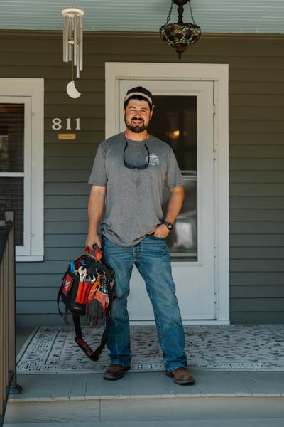 White man with dark brown hair standing on porch. He's wearing a gray shirt with the Nathan's Home Improvement logo.